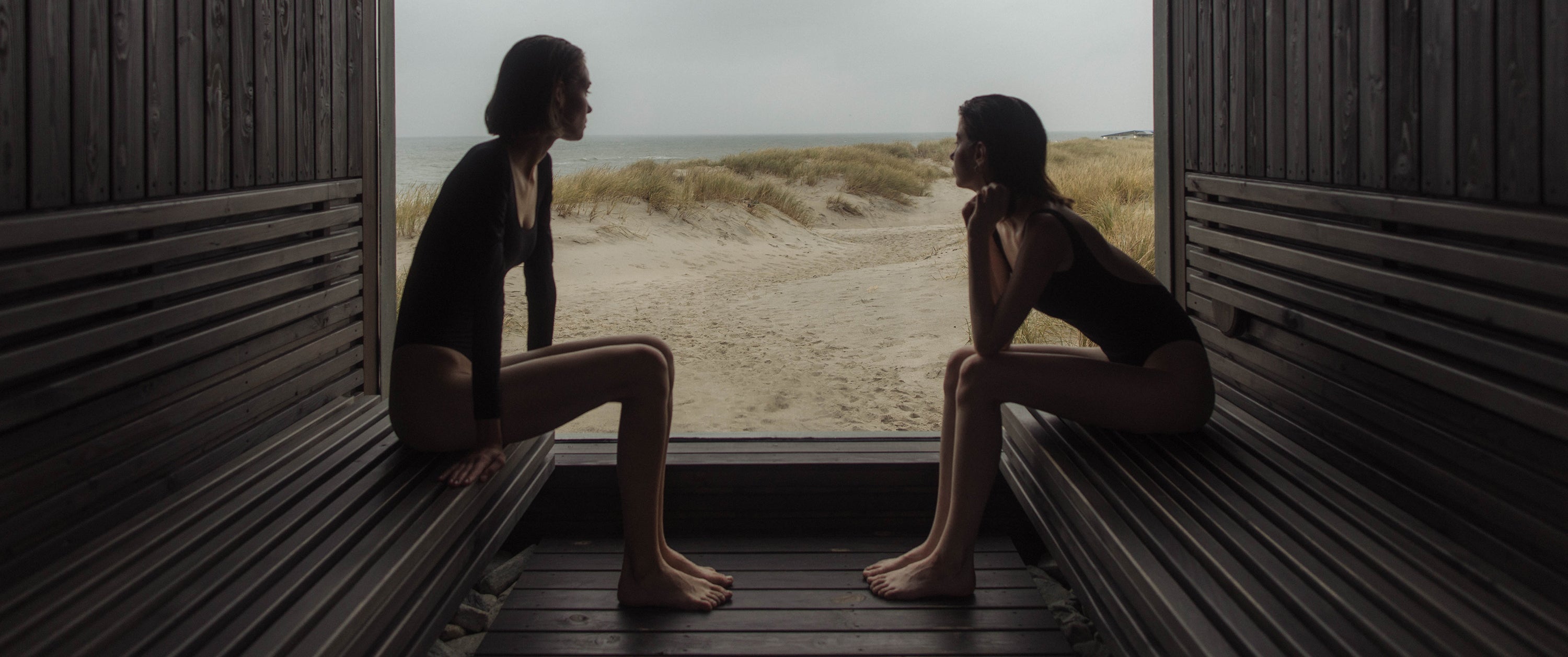 Two women sitting in a sauna and enjoying the beach view.